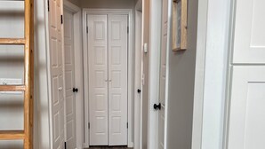 Un couloir avec des portes blanches, un plancher en bois et une échelle en bois appuyée contre le mur.