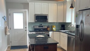 Une cuisine moderne avec des meubles blancs, un îlot central, des appareils en acier inoxydable et un parquet en bois disposé en chevrons.