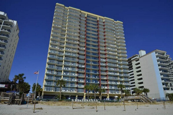A high-rise hotel with multiple balconies, located near a beach.