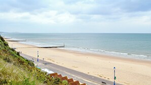 A beach with a road running parallel to it, a pier extending into the water, and a clear sky. - 1 bedroom accommodation in Boscombe, near Bournemouth (Boscombe, near Bournemouth)