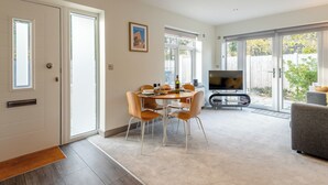 A modern living room with a dining area, a flat-screen TV, and large sliding glass doors leading to a backyard. - 1 bedroom accommodation in Boscombe, near Bournemouth (Boscombe, near Bournemouth)