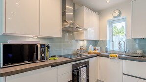 A modern kitchen with white cabinets, a microwave, oven, and a window with a view of greenery outside. - 1 bedroom accommodation in Boscombe, near Bournemouth (Boscombe, near Bournemouth)