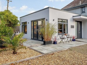 A modern building with large windows, a patio area with seating, and a variety of plants.