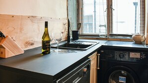 Une cuisine avec une bouteille de vin, des verres, un évier et un lave-linge.