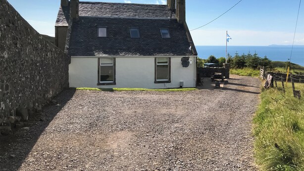 Une maison blanche avec une allée en gravier, un mur de pierre et une vue sur la mer.