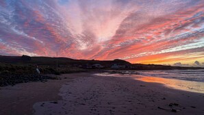Ein Strand mit Sonnenuntergang, Häuser im Hintergrund und einem klaren Himmel.