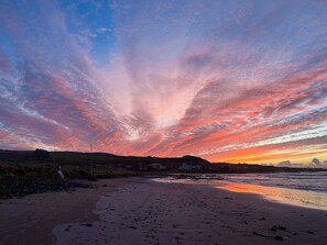 Una playa con un atardecer, casas al fondo y un cielo despejado.