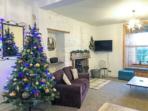 Un salon avec une cheminée, un téléviseur fixé au mur et un sapin de Noël.