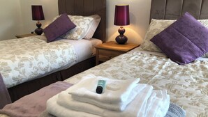 Ein Hotelzimmer mit zwei Betten, jeweils mit Kopfteil, einem Nachttisch mit Lampe und einem Stapel Handtücher.