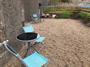 Un patio con suelo de grava, cerca de madera y una mesa de metal con sillas azules.