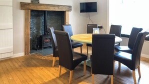 Une pièce avec une table ronde, six chaises, une cheminée, un téléviseur et un mur en pierre.