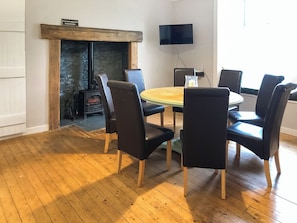 Una habitación con una mesa redonda, seis sillas, una chimenea, un televisor y una pared de piedra.