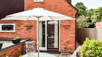 A patio with a glass table and chairs, a white umbrella, and a brick house with a window and door.