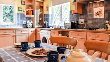 A kitchen with wooden cabinets, a table set with blue cups and a teapot, and a window with a view of greenery.