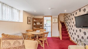 A cozy living room with a dining area, a staircase, and a TV mounted on the wall.