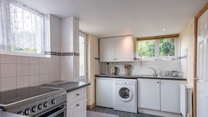 A compact kitchen with white cabinets, a built-in oven, a washing machine, and a window with a view of greenery.