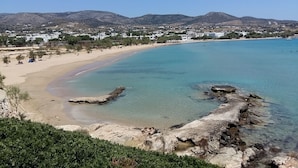 En kustnära strand med klart vatten, klippformationer och en stad i fjärran.