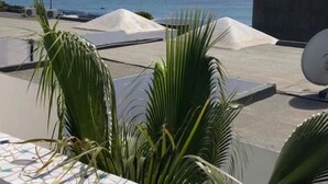 Terraço no telhado com vista para o mar, plantas de palmeira e uma antena parabólica.