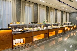 Un buffet garni de divers plats et de différents ustensiles, un sol en marbre et une fenêtre ornée de rideaux légers.