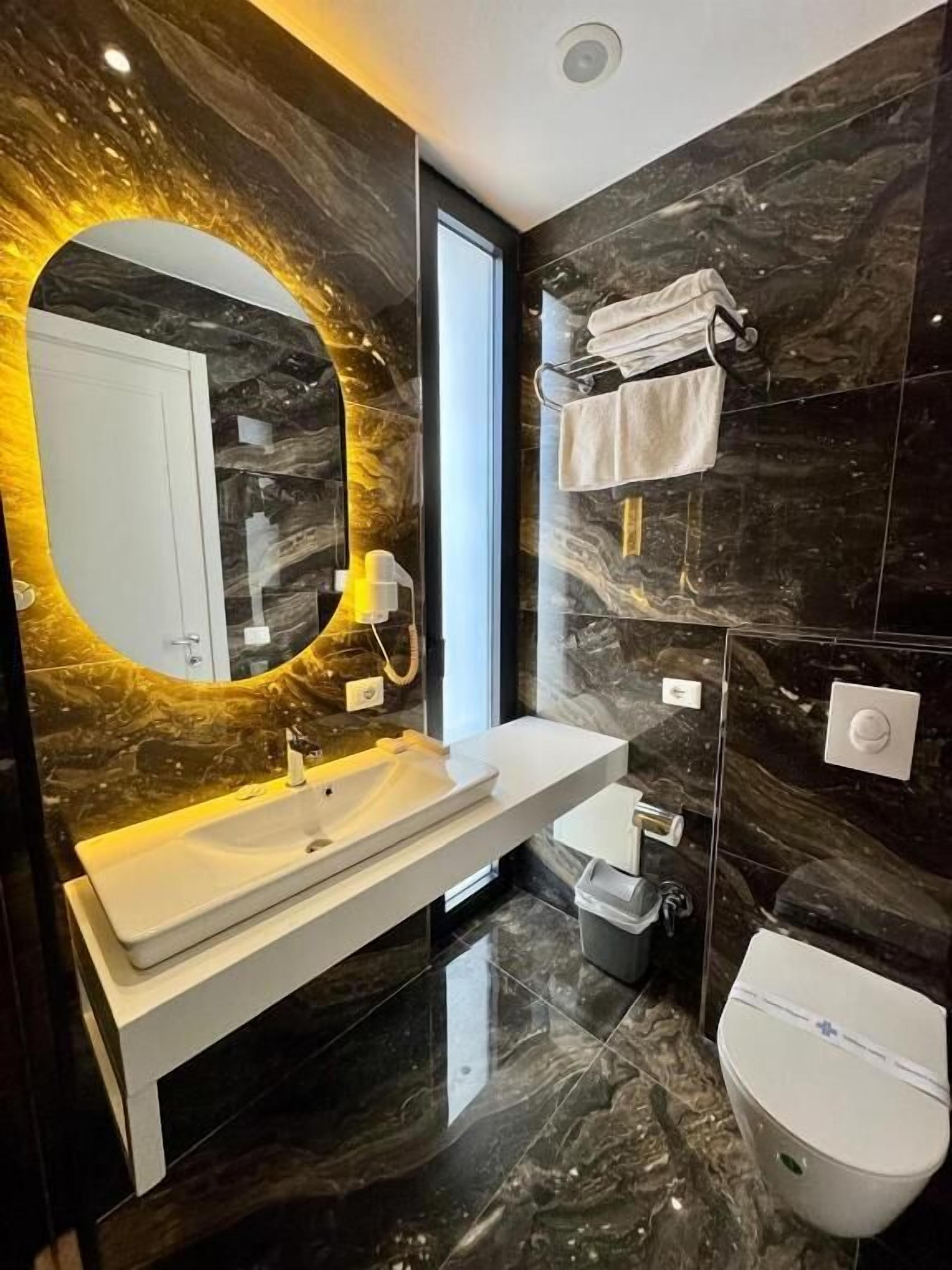A modern bathroom with a marble vanity, a toilet, and a towel rack.