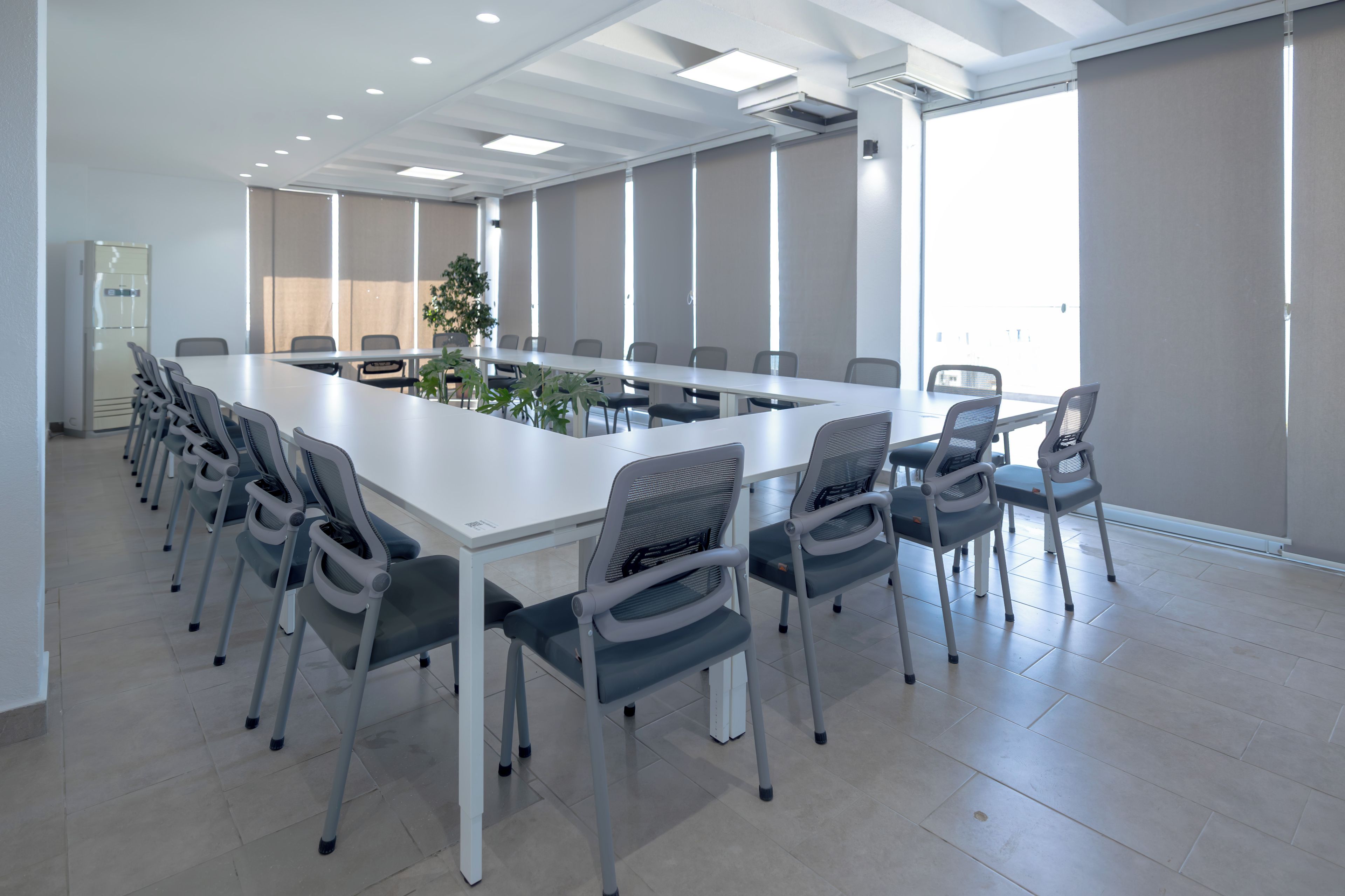 Un salón de conferencias con una larga mesa, sillas y una planta.