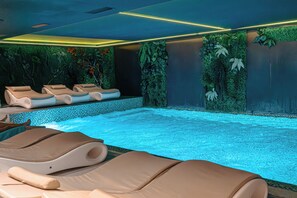 A spa area with a pool, lounge chairs, and a wall decorated with plants. - Henry Resort And Spa  (Golem)