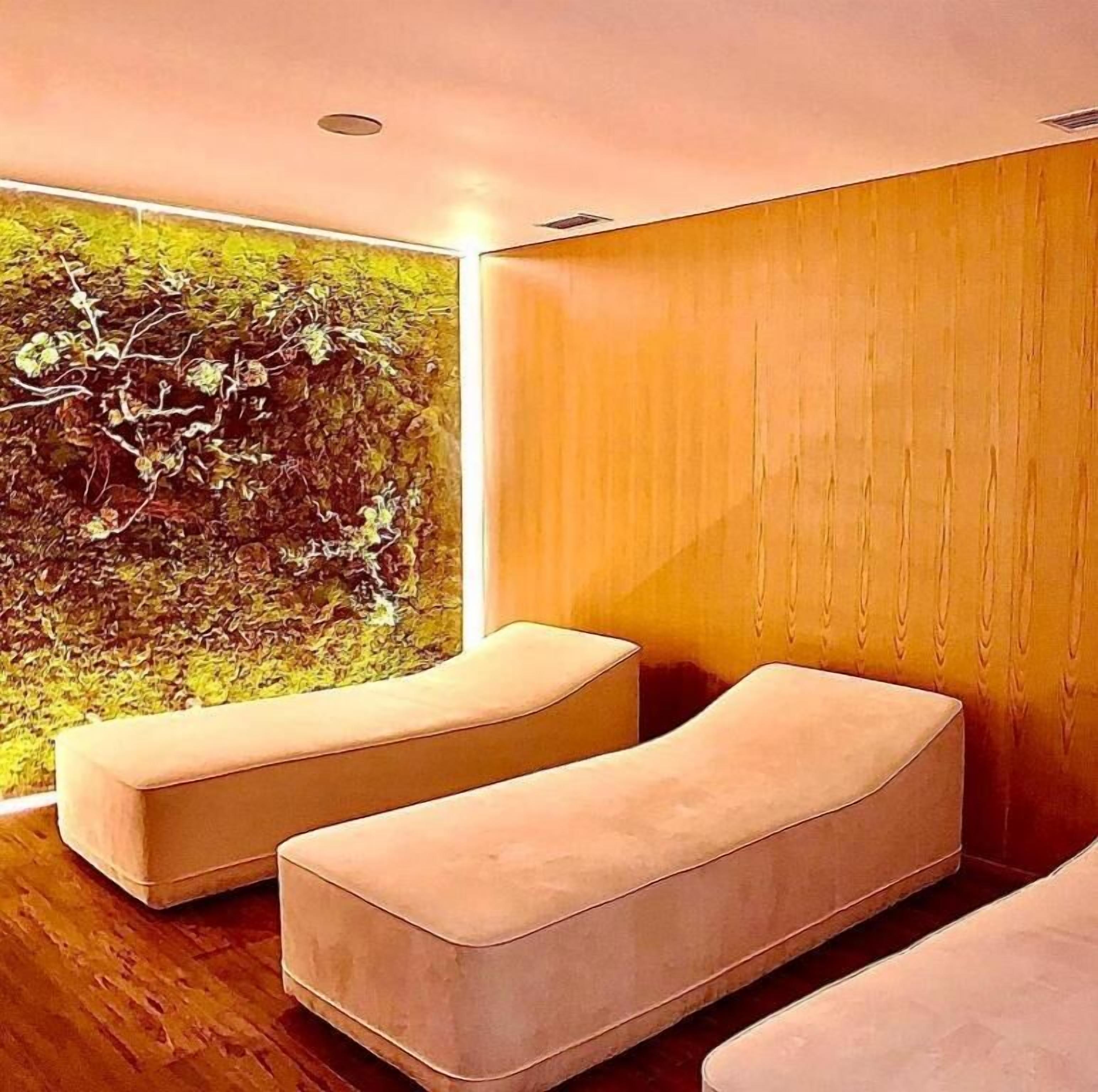 Quarto moderno com parede de madeira e uma janela ampla. Há duas áreas de estar com assentos acolchoados.
