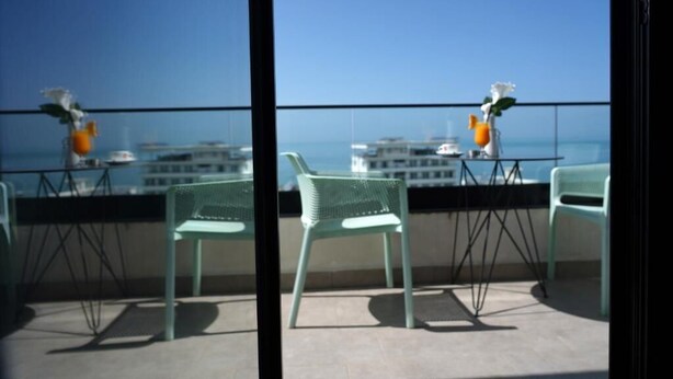 A balcony with two chairs and a table, overlooking a cityscape and the sea. - Henry Resort And Spa  (Golem)