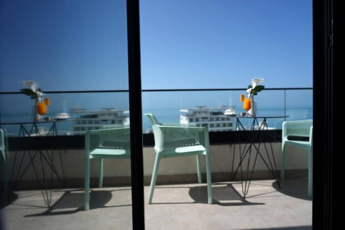 A balcony with two chairs and a table, overlooking a cityscape and the sea.