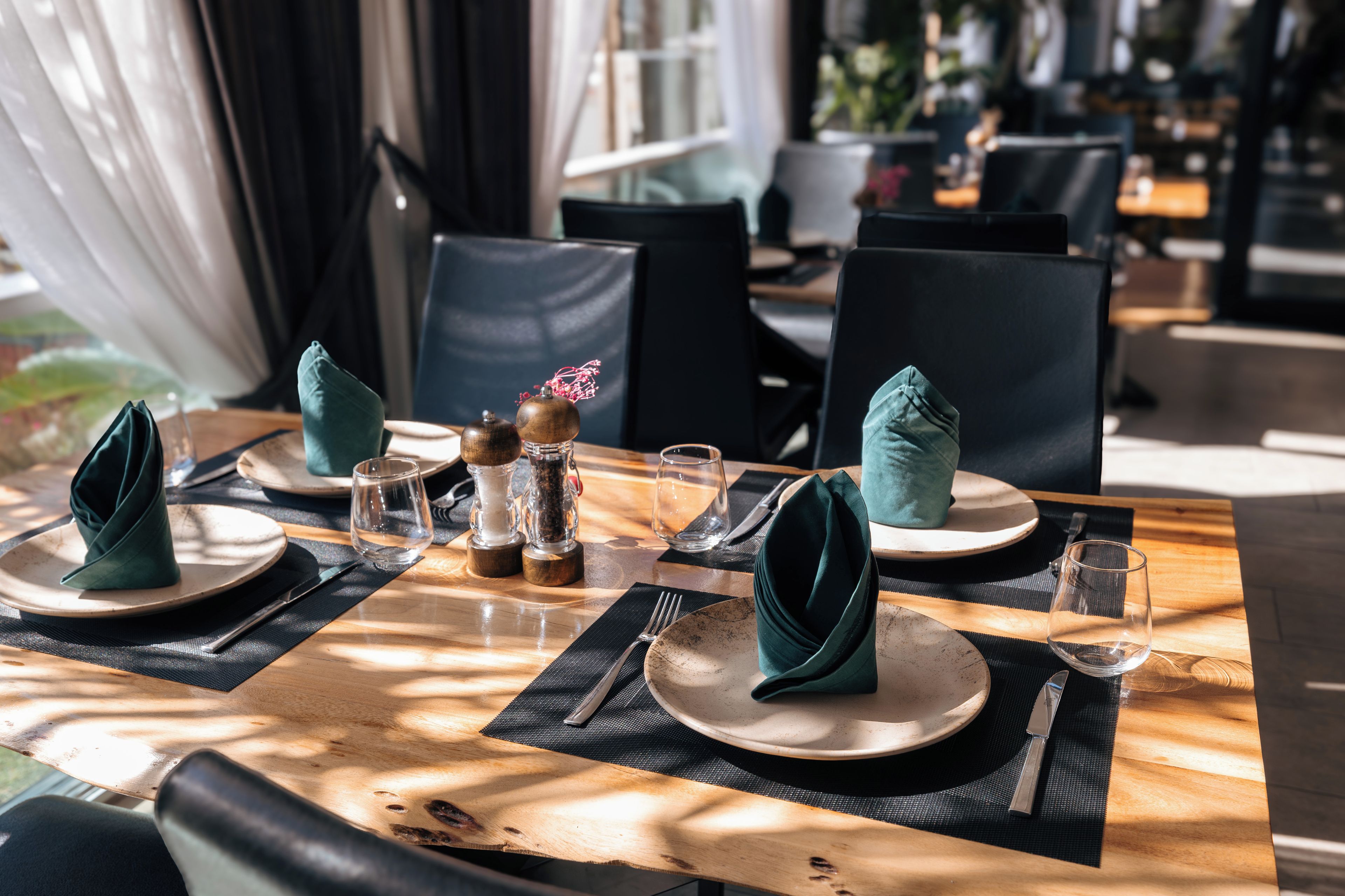 Una mesa de comedor dispuesta con platos, cubiertos y servilletas dobladas.