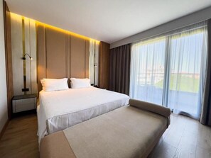 A modern hotel room with a large bed, a bedside table, a lamp, and a large window with curtains. - Henry Resort And Spa  (Golem)