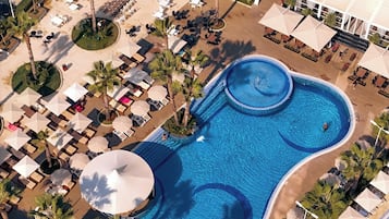 Vista aérea de un complejo turístico con una piscina grande, tumbonas y sombrillas.