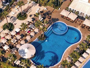 An aerial view of a resort with a large swimming pool, sun loungers, and umbrellas.