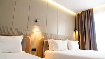 A hotel room with two beds, a headboard with integrated lighting, a wall-mounted light fixture, and a window with curtains.