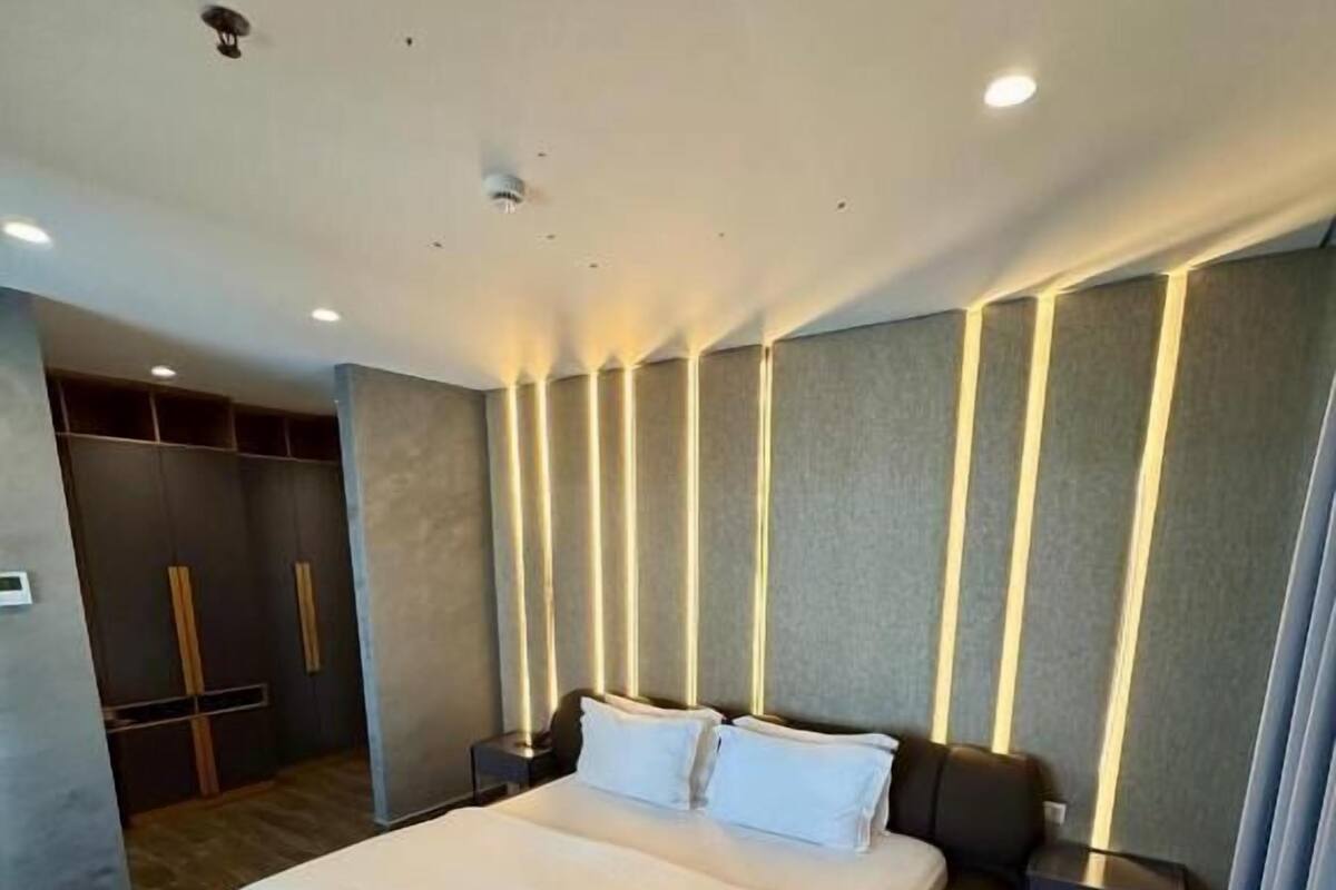 A modern hotel room with a large bed, a wardrobe, a bedside table, and a ceiling light.