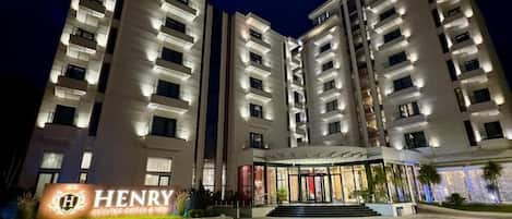 Um hotel com vários andares, entrada imponente, placa de identificação e fachada bem iluminada.