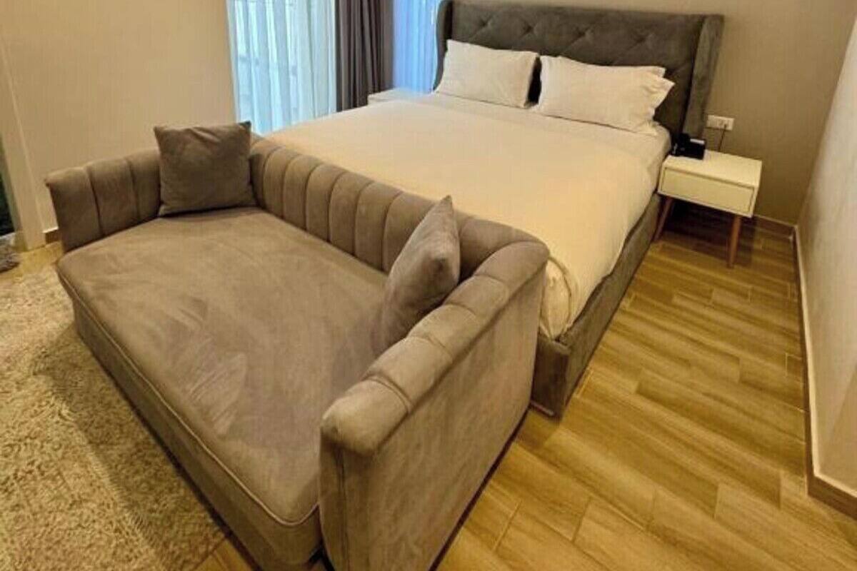 A bedroom with a large bed, a sofa, a nightstand, and a window with curtains.