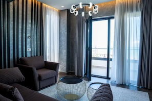 A modern living room with a sofa, a coffee table, and a view of the outdoors through a glass door. - Henry Resort And Spa  (Golem)