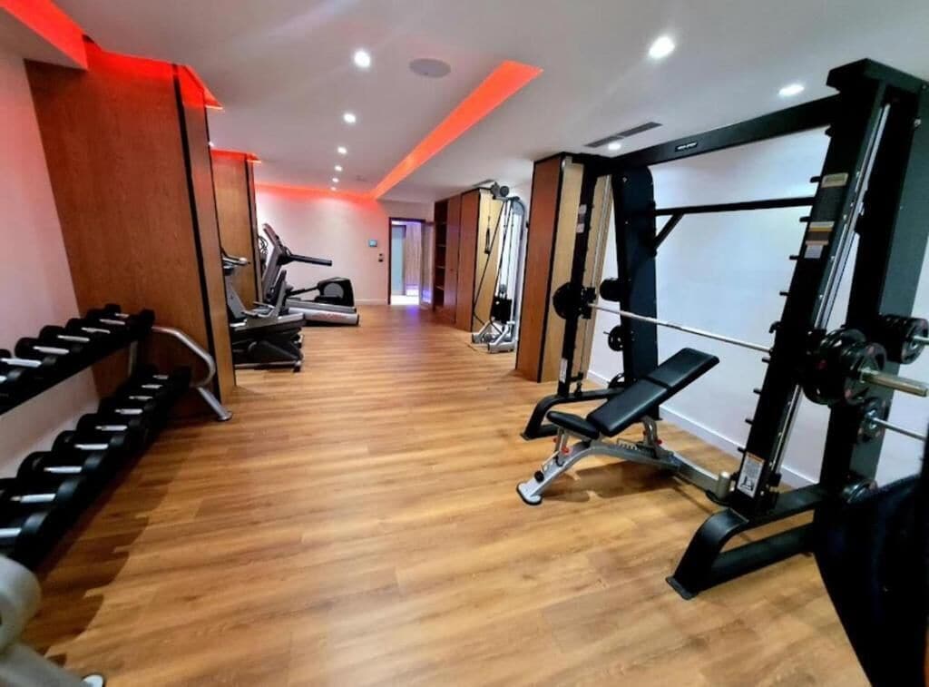 Un gimnasio con máquinas de cardio, pesas libres y una prensa de banca.