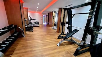 Un gimnasio con máquinas de cardio, pesas libres y una prensa de banca.