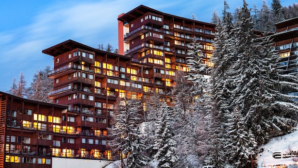 Un hôtel à plusieurs étages, doté de balcons et d’un éclairage chaleureux, entouré d’arbres couverts de neige.