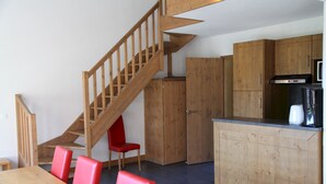 Une cuisine avec des meubles en bois, une cuisinière encastrée et un coin repas comprenant une table en bois et des chaises rouges.