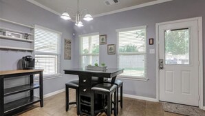 Une cuisine avec une table noire, deux tabourets de bar, une machine à café et une étagère ornée d’objets décoratifs.
