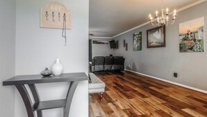 Un salon moderne avec un plancher en bois, un canapé blanc, une table basse en bois foncé et un lustre.
