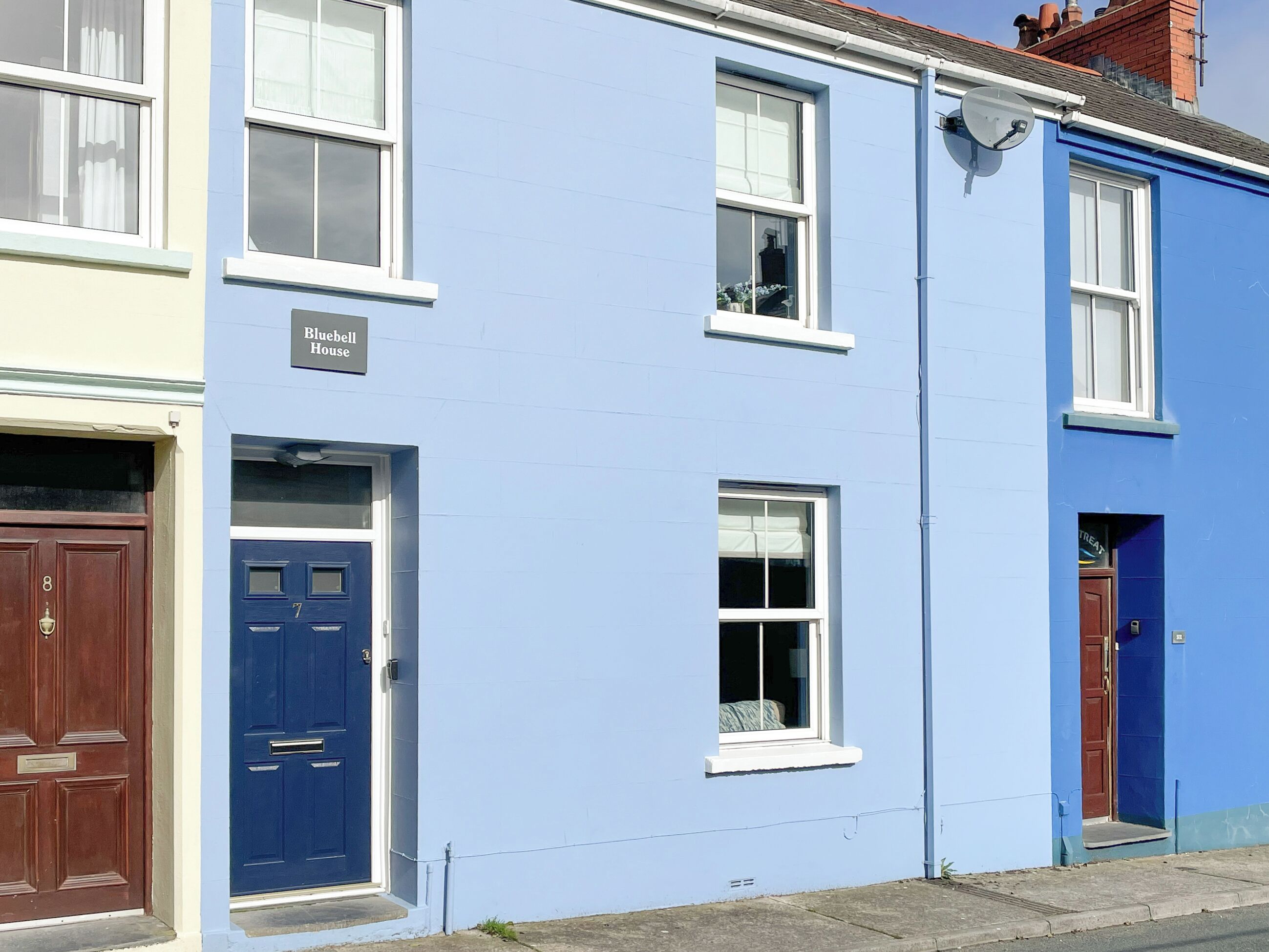 Una hilera de casas adosadas con fachadas de azul y crema, números en las puertas y una antena parabólica visible.