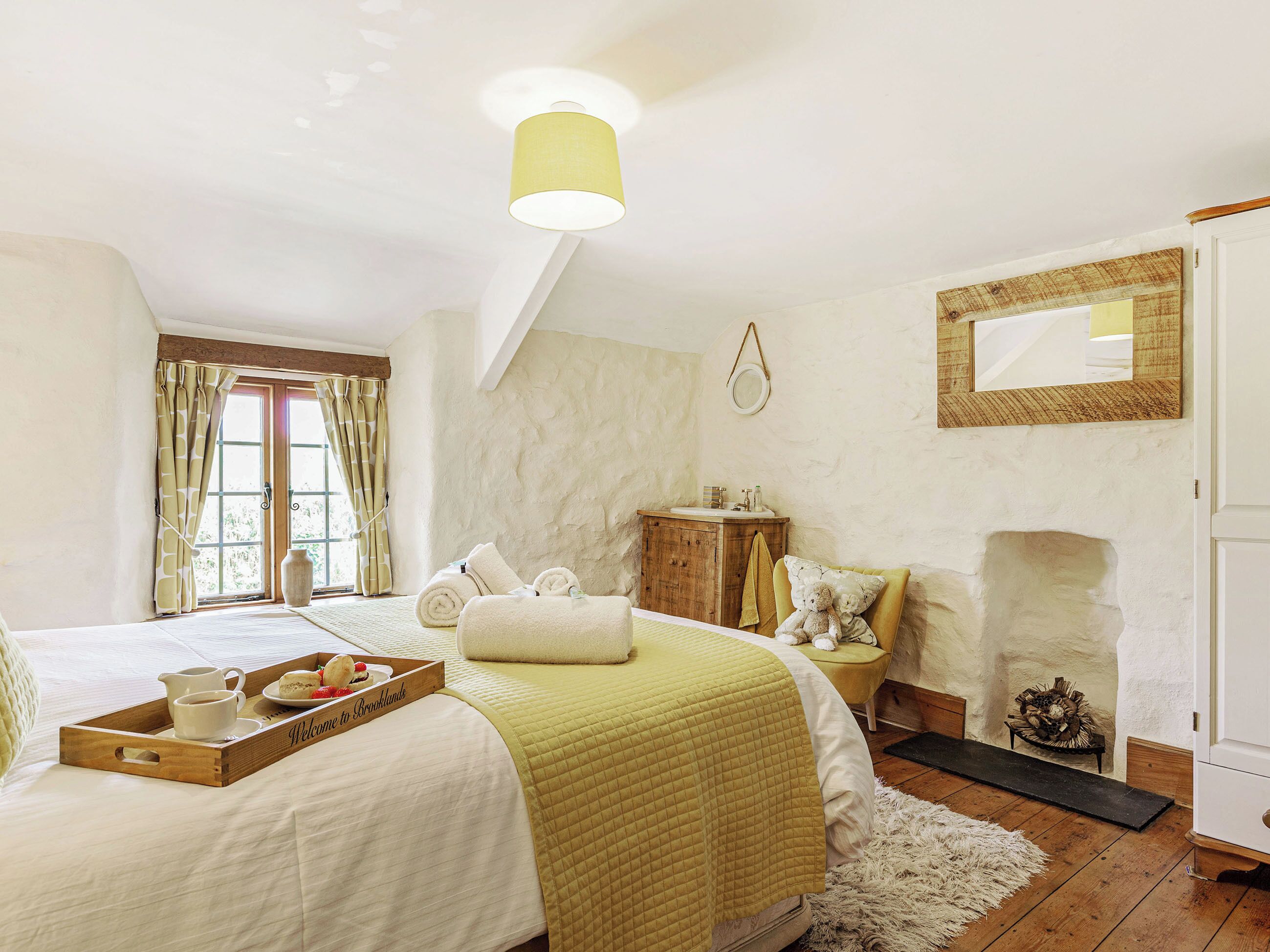 A bedroom with a bed, a bedside table, a mirror, a fireplace, and a window with curtains.