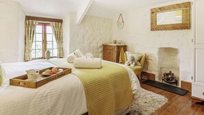 A bedroom with a bed, a bedside table, a mirror, a fireplace, and a window with curtains. - A charming, detached farmhouse with plenty of character. (St Columb Major)