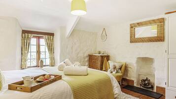 A bedroom with a bed, a bedside table, a mirror, a fireplace, and a window with curtains.