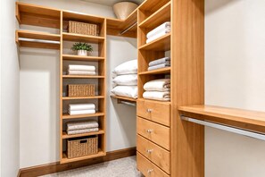 A wooden closet with multiple shelves and drawers, containing folded towels and wicker baskets.