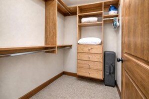 Ein begehbarer Kleiderschrank mit Holzregalen, ein Bett mit weißer Bettwäsche und ein schwarzer Koffer.